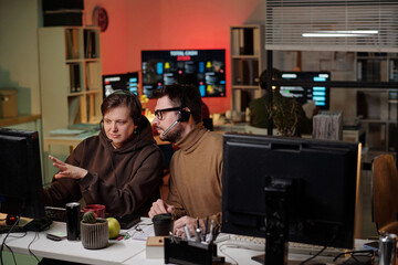Two young adult Caucasian people wearing headsets sitting at desks using computers in office...