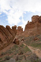 Fototapeta premium A winding path leads through dramatic rock formations and cliffs in Charyn Canyon under a partly cloudy sky