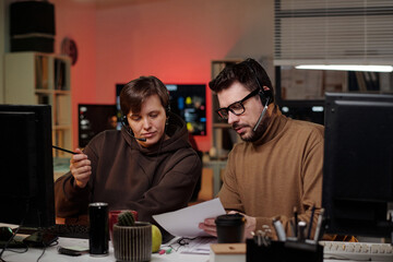 Young adult Caucasian woman and young adult Caucasian man wearing headsets sitting at desks...