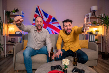 Two friends cheer while watching sports at home with drinks