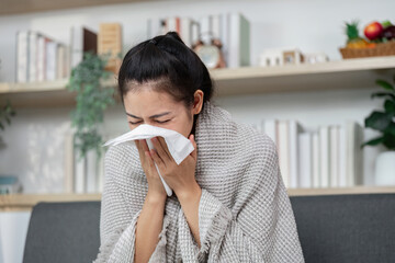 Flu Symptoms. Young woman blowing her nose with a tissue while sitting at home.