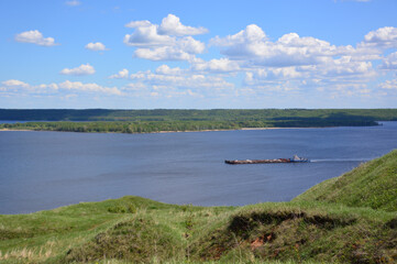 Serene river landscape with a barge under a cloudy blue sky
