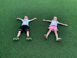 A boy and a girl, twins, are enjoying playing on the green artificial grass soccer field under the summer sun.