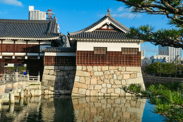 Turret of historic Hiroshima Castle stands on its massive stone foundation, perfectly reflected in tranquil moat. Peaceful scene in Hiroshima, Japan, contrasts ancient architecture with modern city