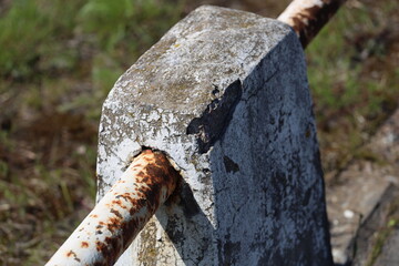 A rusty metal piece sits atop a gray cement block, withered and worn