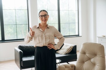 Thumb up hand gesture. Woman in formal clothes is in the modern big room
