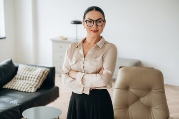 Arms crossed, standing. Woman in formal clothes is in the modern big room