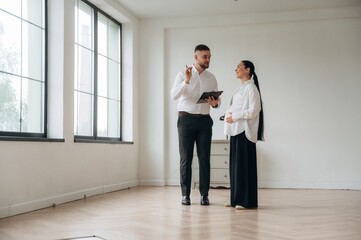 Notepad in hand, showing interior. Man and woman are in the modern new room, conception of business