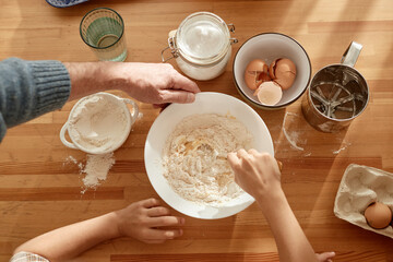 Man and kids cooking together in kitchen, hands mixing flour and eggs in bowl, baking ingredients...