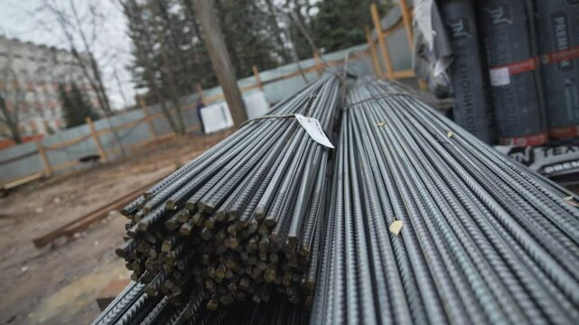 Steel rebar bundles rest on sandy surface awaiting use. Sunlight highlights rusty texture and linear pattern. Building base starts here