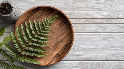 Minimalist composition featuring fern leaf on wooden plate and textured surface