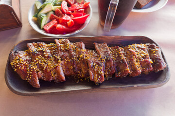 Baked pork ribs under honey mustard sauce on wooden tray