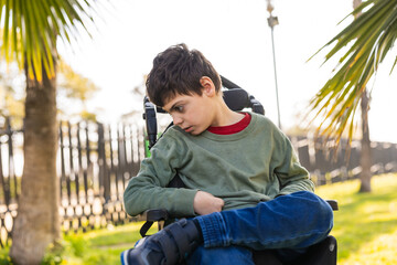 child with disability sitting in wheelchair looking down in park