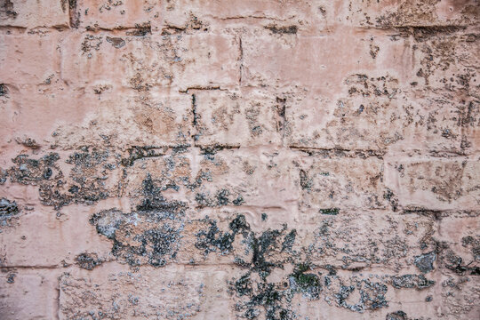 Paint peeling from faded pink brick wall