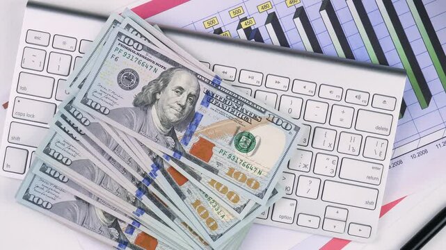 A stack of American dollars falls on a laptop keyboard. Slow motion.