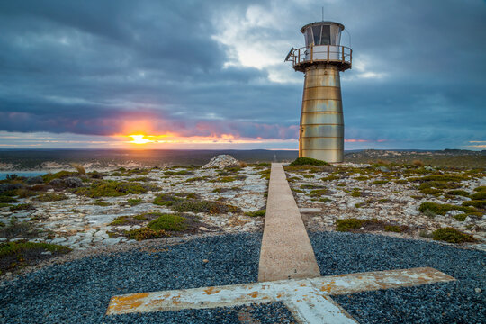 A helipad and a lighthouse on a clifftop at sunrise