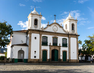 Brazilian colonial church with white walls and green details under a vibrant blue sky.