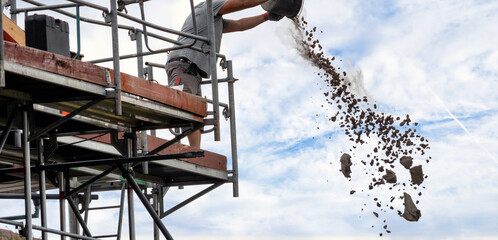A construction worker disposes rubble from a bucket on a tall scaffold during a renovation project