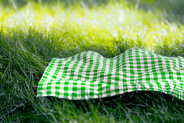 Green checked picnic napkin,tablecloth on grass empty food advertisement space. Plaid checkered towel, cloth.Summertime template.
