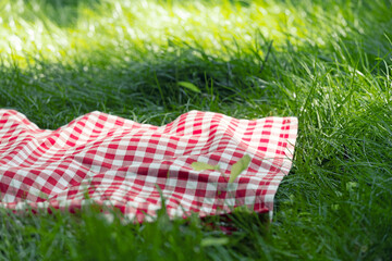 Red checkered picnic towel plaid on grass, tablecloth outdoors.Food advertisement summer backdrop.