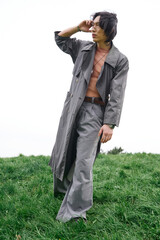 Young man showcases modern fashion in grey outfit while strolling through tranquil park