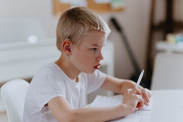 Fototapeta premium Young mother helps her hard-of-hearing son with schoolwork at home. A natural, heartfelt moment of inclusion, care, and rehabilitation, highlighting love, support, and everyday learning