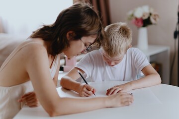 Young mother helps her hard-of-hearing son with schoolwork at home. A natural, heartfelt moment of...