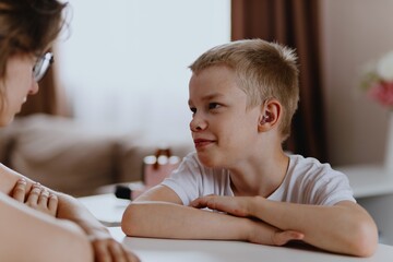 Young mother helps her hard-of-hearing son with schoolwork at home. A natural, heartfelt moment of...