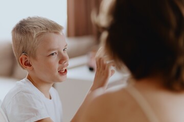 Young mother helps her hard-of-hearing son with schoolwork at home. A natural, heartfelt moment of...