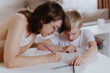 Young mother helps her hard-of-hearing son with schoolwork at home. A natural, heartfelt moment of...