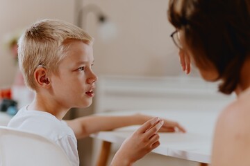 Young mother helps her hard-of-hearing son with schoolwork at home. A natural, heartfelt moment of...