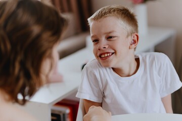 Young mother helps her hard-of-hearing son with schoolwork at home. A natural, heartfelt moment of...