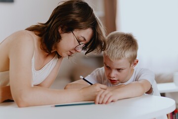Young mother helps her hard-of-hearing son with schoolwork at home. A natural, heartfelt moment of...