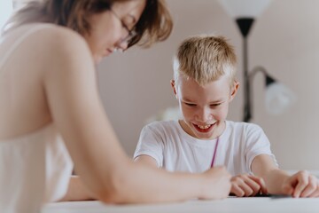 Young mother helps her hard-of-hearing son with schoolwork at home. A natural, heartfelt moment of...