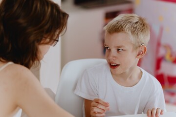 Young mother helps her hard-of-hearing son with schoolwork at home. A natural, heartfelt moment of...