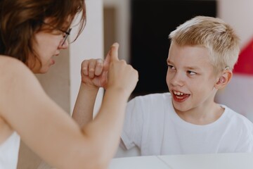 Young mother helps her hard-of-hearing son with schoolwork at home. A natural, heartfelt moment of...