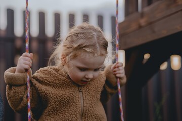 Beautiful 3-year-old girl playing on a neighborhood playground swinging, running on the grass, and enjoying fresh air. A joyful, natural moment full of real emotions and unaltered beauty