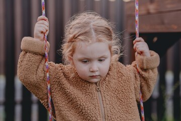 Beautiful 3-year-old girl playing on a neighborhood playground swinging, running on the grass, and enjoying fresh air. A joyful, natural moment full of real emotions and unaltered beauty