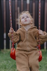 Beautiful 3-year-old girl playing on a neighborhood playground swinging, running on the grass, and enjoying fresh air. A joyful, natural moment full of real emotions and unaltered beauty