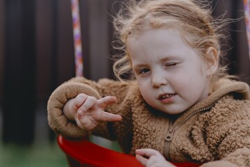 Beautiful 3-year-old girl playing on a neighborhood playground swinging, running on the grass, and enjoying fresh air. A joyful, natural moment full of real emotions and unaltered beauty