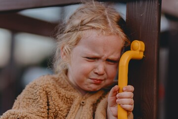 Beautiful and active 3-year-old girl plays on a neighborhood playground but becomes upset and starts crying. A raw, unaltered moment capturing real childhood emotions in a natural outdoor