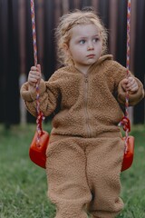 Beautiful 3-year-old girl playing on a neighborhood playground swinging, running on the grass, and enjoying fresh air. A joyful, natural moment full of real emotions and unaltered beauty