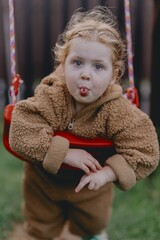 Beautiful 3-year-old girl playing on a neighborhood playground swinging, running on the grass, and enjoying fresh air. A joyful, natural moment full of real emotions and unaltered beauty