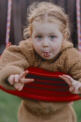 Beautiful 3-year-old girl playing on a neighborhood playground swinging, running on the grass, and enjoying fresh air. A joyful, natural moment full of real emotions and unaltered beauty