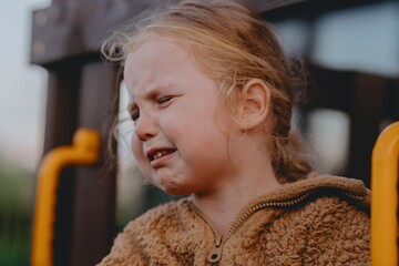 Beautiful and active 3-year-old girl plays on a neighborhood playground but becomes upset and starts crying. A raw, unaltered moment capturing real childhood emotions in a natural outdoor