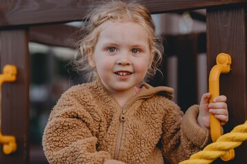 Beautiful 3-year-old girl playing on a neighborhood playground swinging, running on the grass, and enjoying fresh air. A joyful, natural moment full of real emotions and unaltered beauty