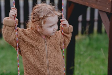 Beautiful 3-year-old girl playing on a neighborhood playground swinging, running on the grass, and enjoying fresh air. A joyful, natural moment full of real emotions and unaltered beauty