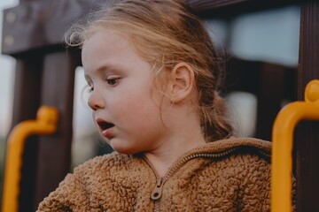 Beautiful 3-year-old girl playing on a neighborhood playground swinging, running on the grass, and enjoying fresh air. A joyful, natural moment full of real emotions and unaltered beauty