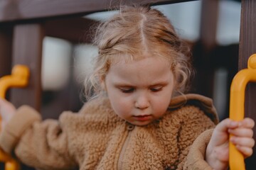 Beautiful 3-year-old girl playing on a neighborhood playground swinging, running on the grass, and enjoying fresh air. A joyful, natural moment full of real emotions and unaltered beauty
