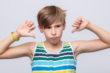 Young boy expresses disappointment with thumbs down gesture against a light background